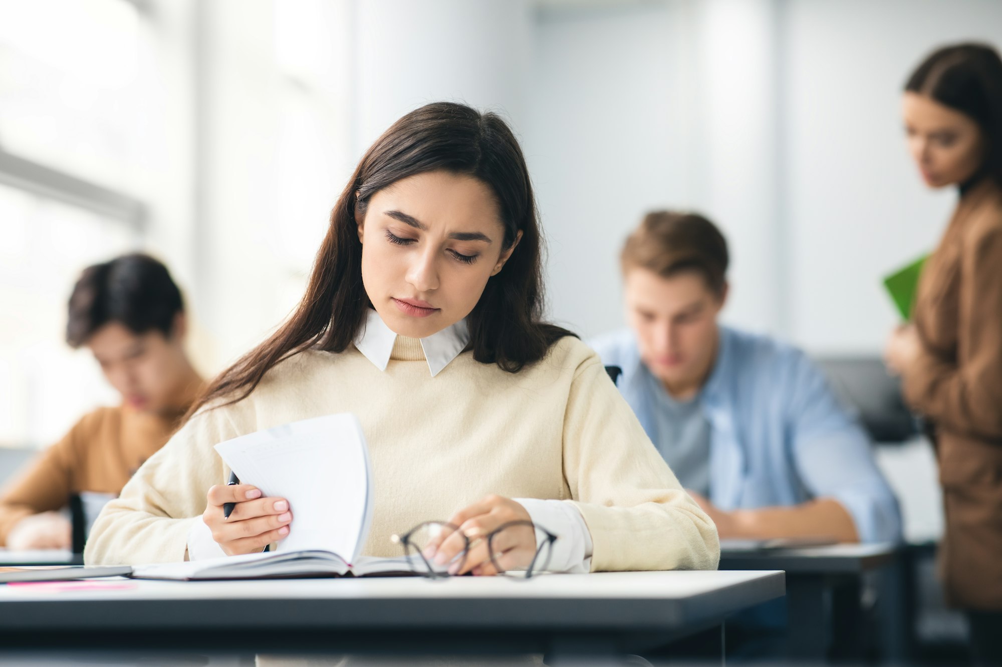 Female student sitting at desk in classroom writing exam